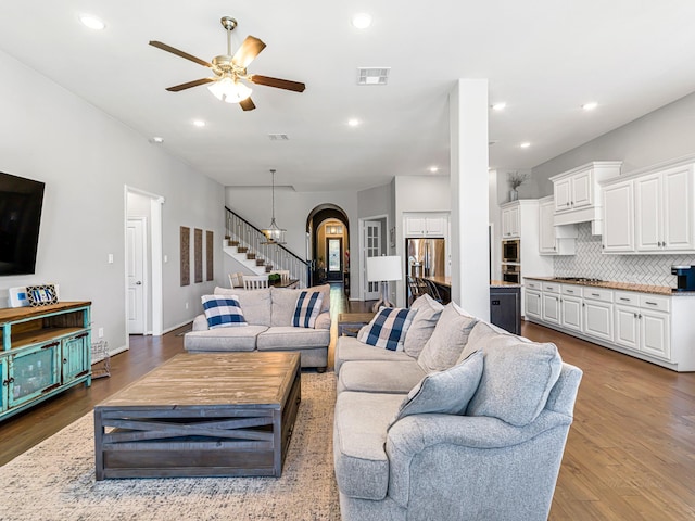 living area with arched walkways, recessed lighting, visible vents, stairway, and wood finished floors