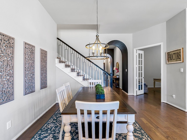 dining area featuring arched walkways, a chandelier, wood finished floors, baseboards, and stairs