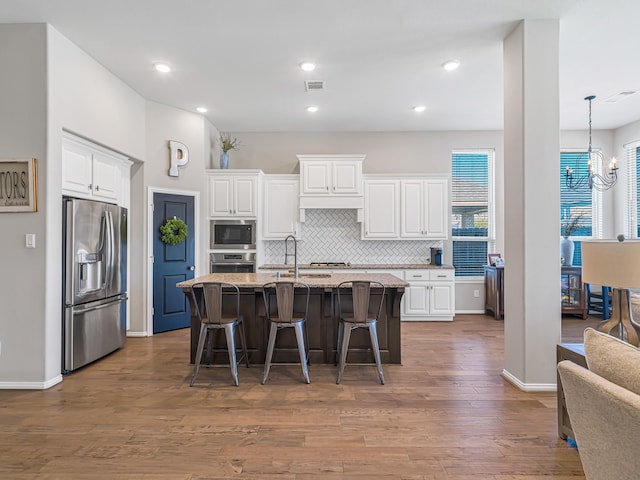 kitchen featuring visible vents, a kitchen breakfast bar, stainless steel appliances, a chandelier, and backsplash