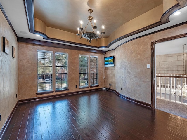 empty room with baseboards, a raised ceiling, wood-type flooring, crown molding, and a notable chandelier