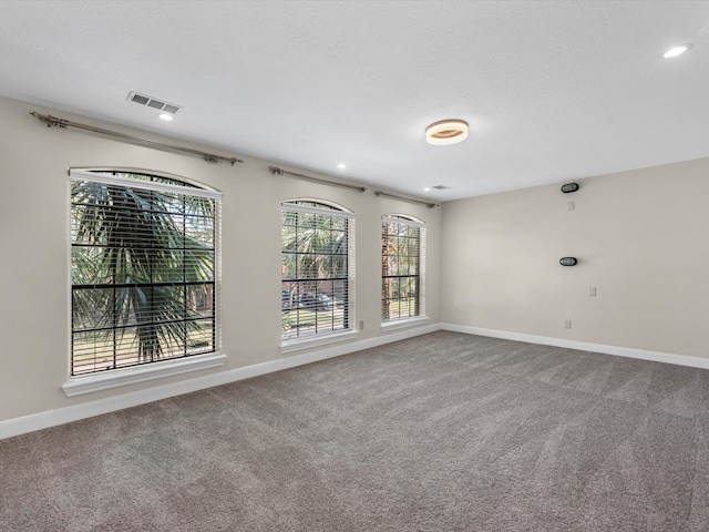 carpeted spare room with visible vents, a textured ceiling, and baseboards