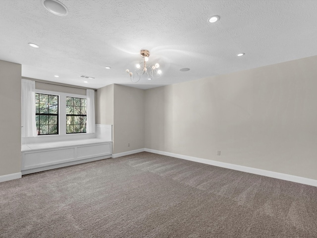 carpeted spare room with a textured ceiling, a notable chandelier, visible vents, and baseboards