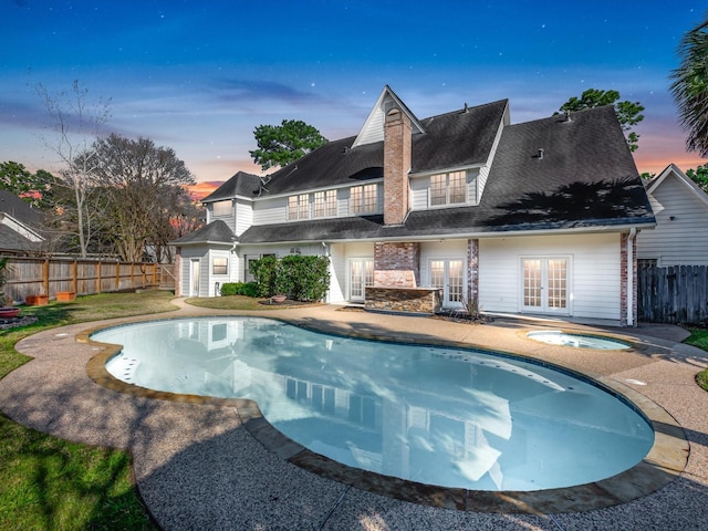 pool at dusk featuring an in ground hot tub, french doors, a fenced backyard, and a fenced in pool