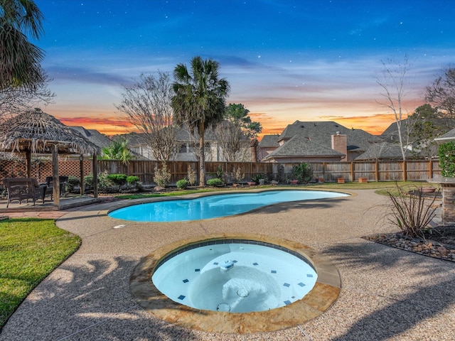 pool at dusk featuring a fenced in pool, a patio area, a fenced backyard, and an in ground hot tub