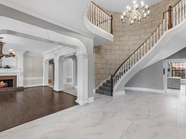 foyer entrance featuring marble finish floor, a fireplace, ornate columns, a high ceiling, and baseboards