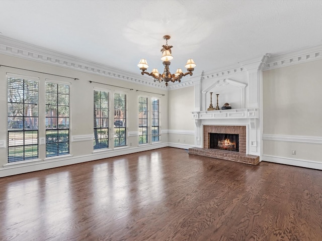 unfurnished living room with an inviting chandelier, a brick fireplace, ornamental molding, and dark wood finished floors