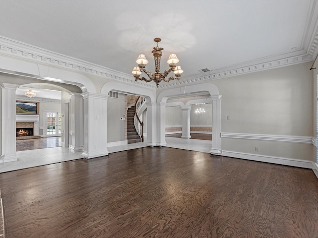 spare room with arched walkways, decorative columns, a lit fireplace, and an inviting chandelier