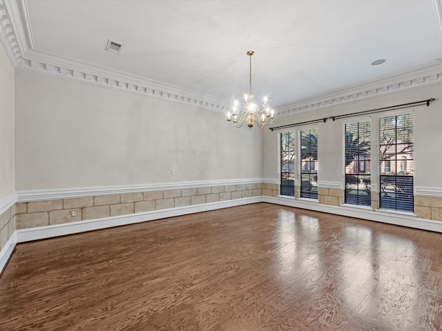 empty room with a notable chandelier, visible vents, wood finished floors, and ornamental molding