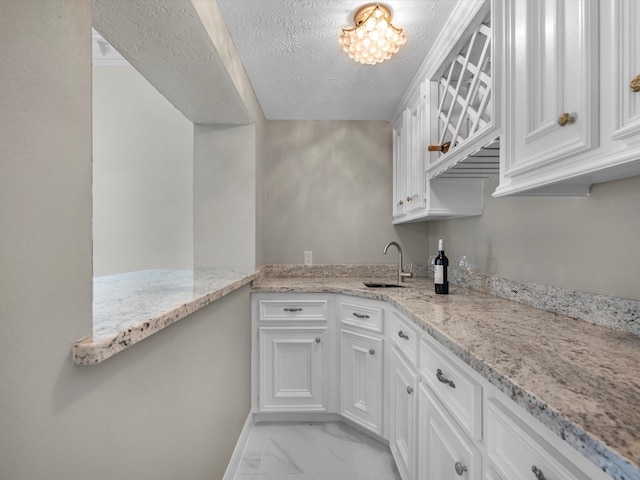 7714 Hertfordshire Dr, Spring, TX 77379 - kitchen with a sink, a textured ceiling, white cabinets, light marble finish flooring, and light stone countertops