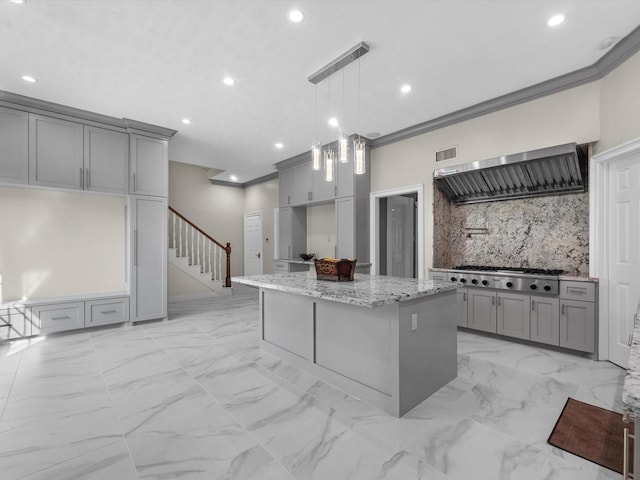 kitchen featuring gray cabinetry, marble finish floor, ornamental molding, wall chimney range hood, and decorative backsplash