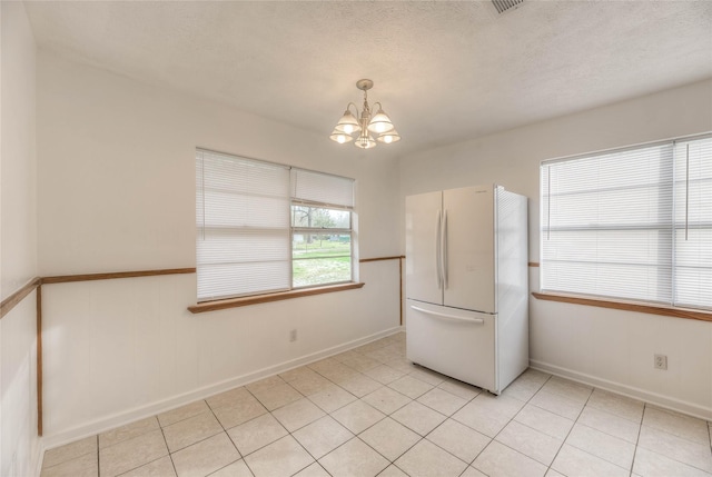 interior space with a textured ceiling, light tile patterned floors, baseboards, and an inviting chandelier