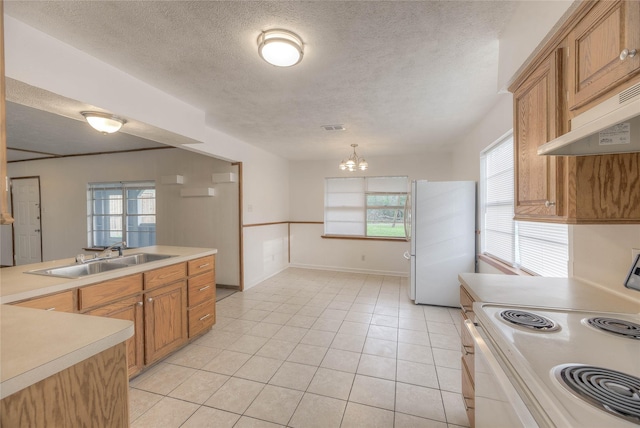 kitchen featuring white appliances, light countertops, a textured ceiling, under cabinet range hood, and a sink