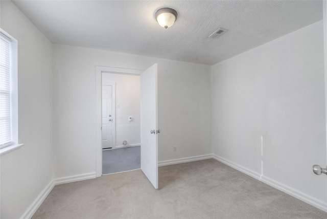 empty room featuring light carpet, baseboards, visible vents, and a textured ceiling