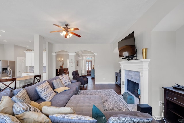 living room featuring arched walkways, a ceiling fan, dark wood-type flooring, vaulted ceiling, and a fireplace