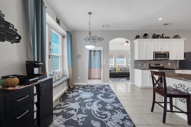 kitchen featuring arched walkways, light tile patterned floors, stainless steel appliances, visible vents, and backsplash