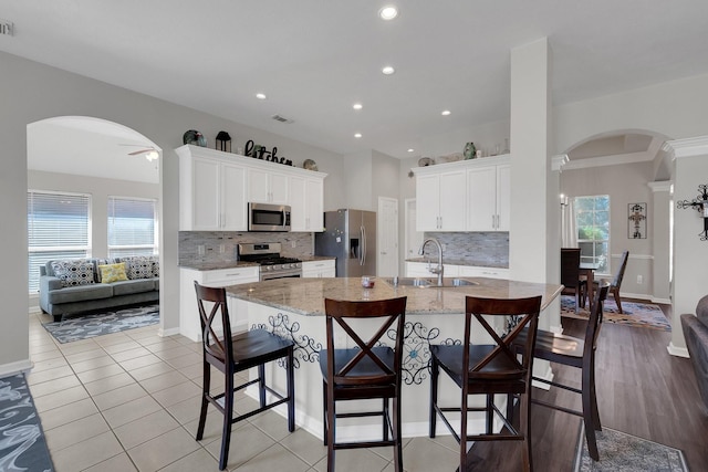 kitchen featuring arched walkways, a breakfast bar, a sink, white cabinets, and appliances with stainless steel finishes