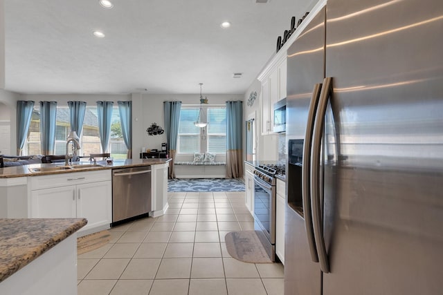 kitchen featuring stone counters, light tile patterned floors, stainless steel appliances, white cabinets, and a sink