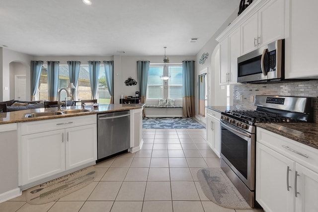 kitchen with arched walkways, light tile patterned floors, tasteful backsplash, appliances with stainless steel finishes, and a sink