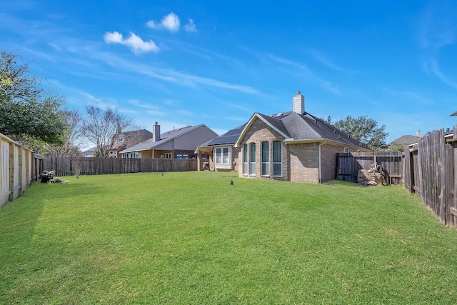 exterior space with a fenced backyard, a chimney, a lawn, and brick siding