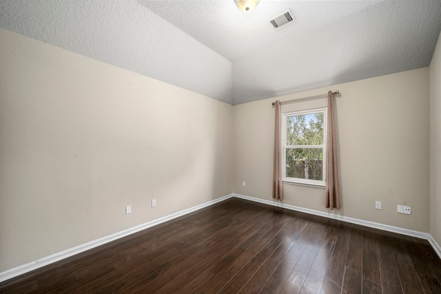 empty room with dark wood-style floors, visible vents, vaulted ceiling, a textured ceiling, and baseboards