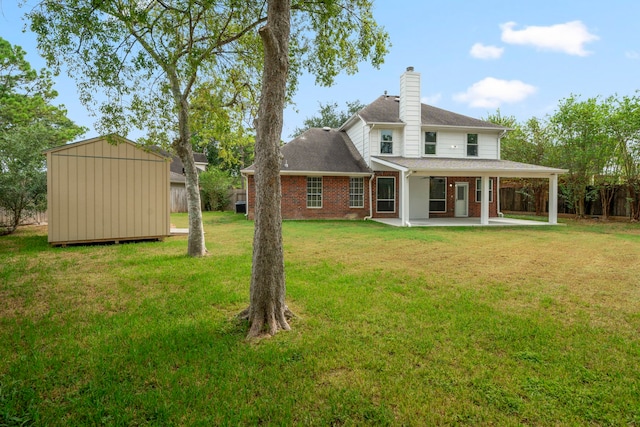 back of house with an outbuilding, brick siding, a yard, a patio, and a chimney