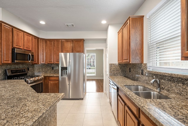 kitchen featuring light stone counters, light tile patterned floors, stainless steel appliances, visible vents, and a sink