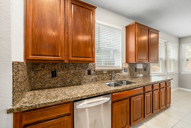 kitchen featuring stone counters, light tile patterned floors, backsplash, stainless steel dishwasher, and a sink