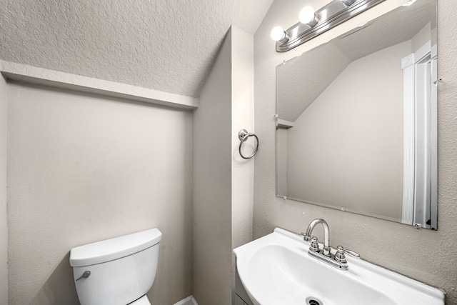 half bath with a textured wall, toilet, lofted ceiling, a textured ceiling, and vanity