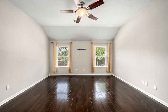 empty room with a textured ceiling, baseboards, vaulted ceiling, and dark wood-style flooring