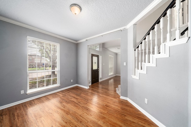 entrance foyer with ornamental molding, stairway, wood finished floors, and baseboards