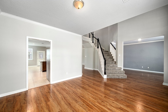 unfurnished room featuring wood finished floors, a textured ceiling, baseboards, and stairs