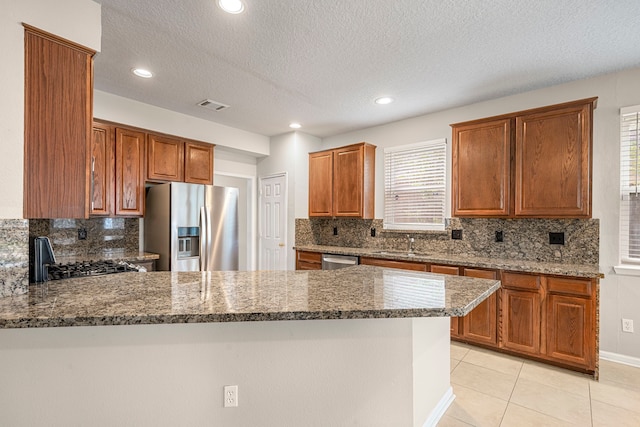 kitchen featuring visible vents, appliances with stainless steel finishes, a sink, dark stone countertops, and a peninsula