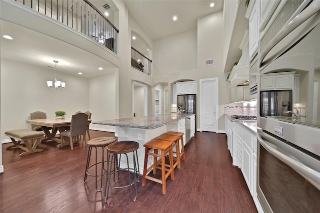 kitchen with arched walkways, white cabinets, dark wood finished floors, light stone counters, and appliances with stainless steel finishes