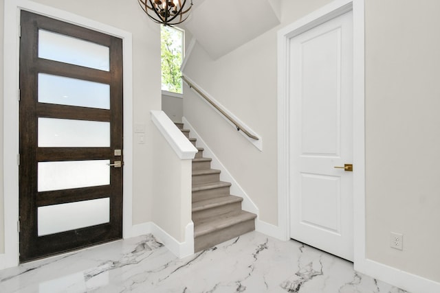 foyer entrance with a notable chandelier, marble finish floor, stairway, and baseboards