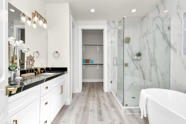 bathroom featuring a marble finish shower, a soaking tub, a spacious closet, vanity, and wood finished floors