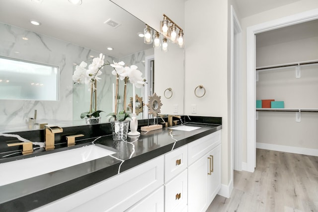 bathroom featuring a walk in closet, double vanity, visible vents, a sink, and wood finished floors