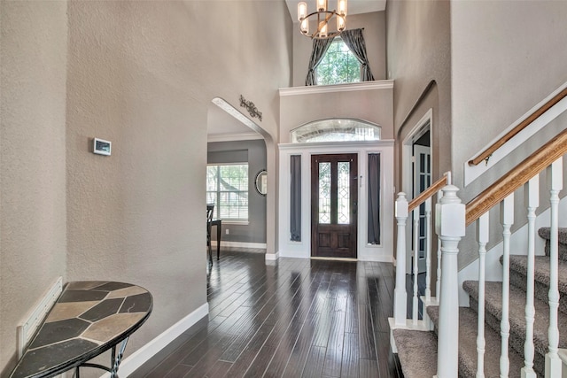 foyer entrance featuring baseboards, a towering ceiling, wood finished floors, stairs, and a notable chandelier