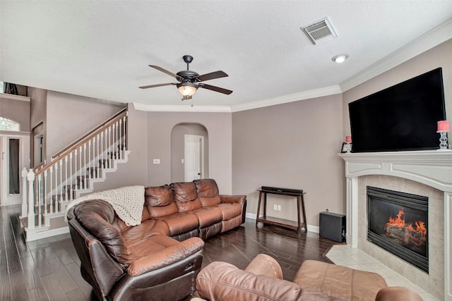 living room with arched walkways, visible vents, a tiled fireplace, wood finished floors, and stairs