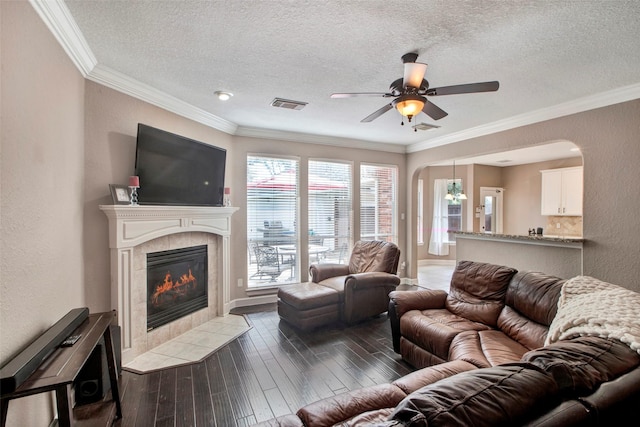 living area with dark wood-style floors, a tile fireplace, visible vents, and crown molding