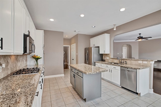 kitchen featuring arched walkways, appliances with stainless steel finishes, a sink, a kitchen island, and a peninsula