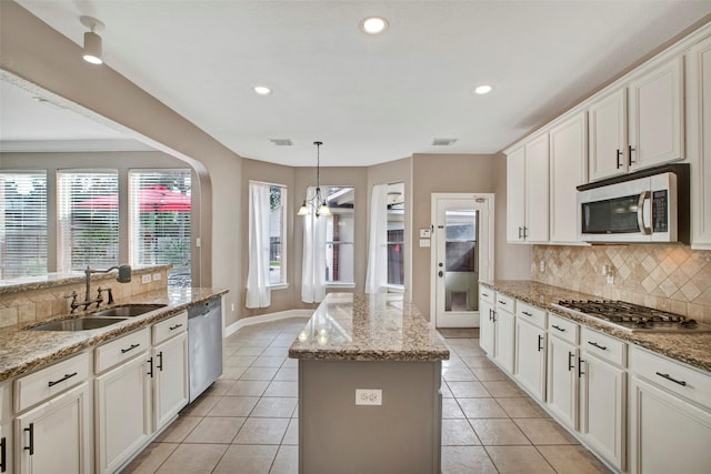 kitchen featuring light tile patterned floors, decorative backsplash, a kitchen island, stainless steel appliances, and a sink