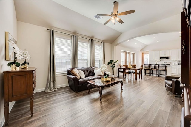 living room with lofted ceiling, ceiling fan, arched walkways, wood finished floors, and visible vents