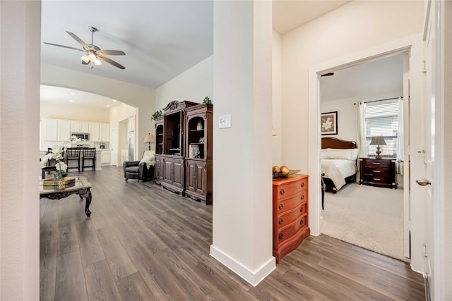 corridor featuring baseboards, arched walkways, and dark wood-style flooring