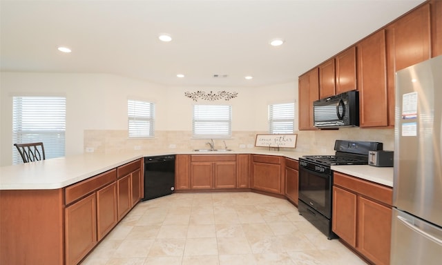 kitchen with a peninsula, a sink, light countertops, a wealth of natural light, and black appliances