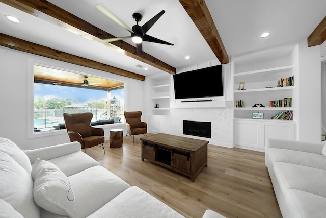 living room featuring a large fireplace, ceiling fan, beamed ceiling, and light wood-style flooring