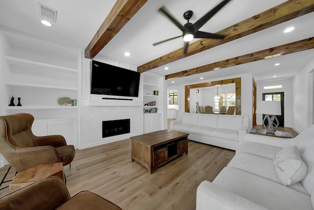 living room with light wood finished floors, visible vents, ceiling fan, beamed ceiling, and a fireplace