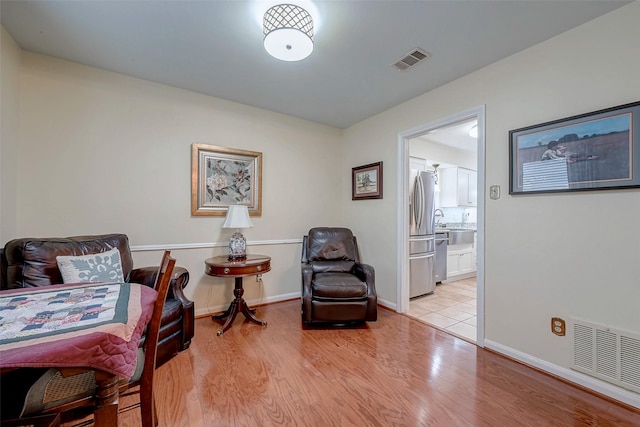 living area featuring visible vents, light wood-style flooring, and baseboards