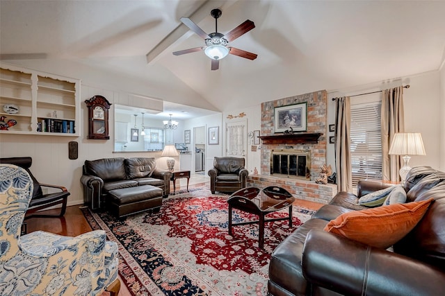 living room featuring lofted ceiling with beams, ceiling fan with notable chandelier, wood finished floors, a healthy amount of sunlight, and a brick fireplace