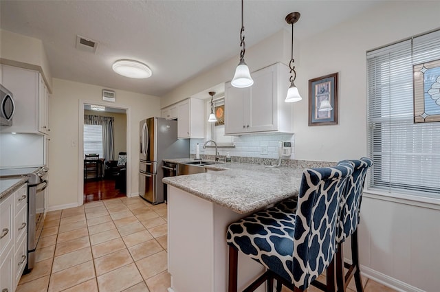 kitchen with visible vents, white cabinets, appliances with stainless steel finishes, a kitchen breakfast bar, and a peninsula