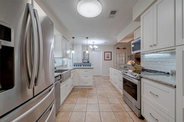 kitchen with light tile patterned flooring, a peninsula, visible vents, white cabinetry, and appliances with stainless steel finishes